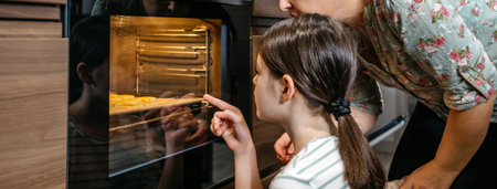 Banner of mother and daughter are carefully watching cookies baking in the oven, anticipating the delicious outcome of work. Young girl pointing with finger to biscuits. Family time cooking concept.の写真素材