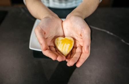 Unrecognizable female pastry chef hands holding a freshly baked heart shaped cookie with egg glaze, showcasing her passion and love for bakingの写真素材