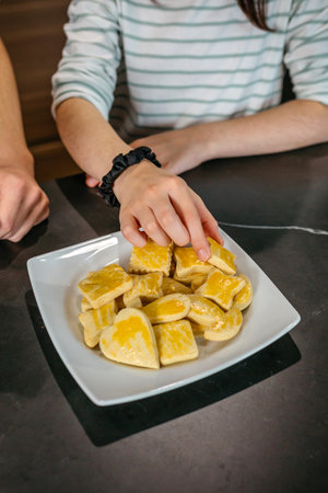 Unrecognizable girl is picking a freshly baked cookie from a white plate on a kitchen countertop next to another child hands waiting to eat.の写真素材