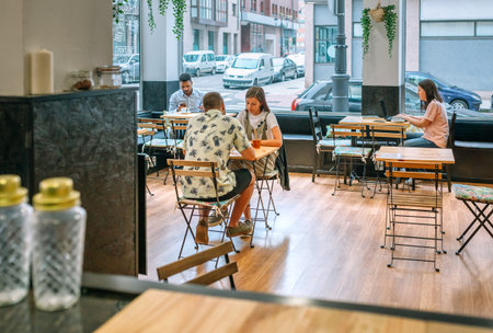 Customers enjoying coffee and working on laptops in a bright, inviting cafe, capturing the essence of modern cafe culture and urban lifestyle in a lively and social atmosphereの写真素材