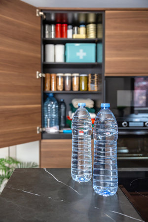 Water bottles in front of survival pantry stored according to government recommendations about emergency or war preparedness. Cupboard with food, drink, first aid supplies and clothes in kitchen.の写真素材
