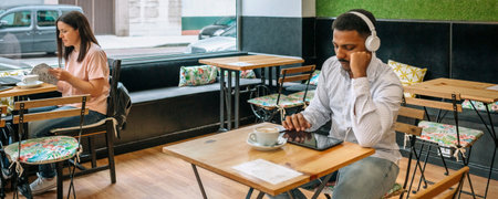 Banner of freelancers working at various tables, engaging with their devices and sipping coffee in a modern cafe featuring large windows, embodying urban life and creativityの写真素材