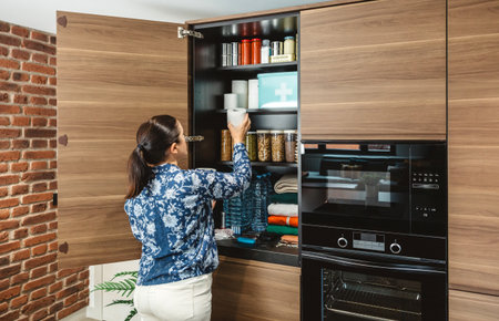 Unrecognizable female filling toilet paper to stocked emergency food pantry in kitchen, preparing for potential disasters. 72 hours survival kit concept. Alert, foresight and self sufficiency strategyの写真素材