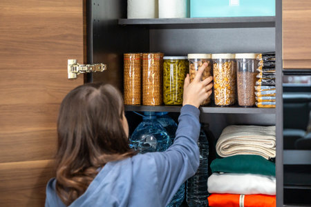 Unrecognizable girl storing peanuts container in emergency food storage pantry. 72 hour survival kit with water, cookies, pasta, beans, legumes, cereals and water ready for disasters or food shortage.の写真素材