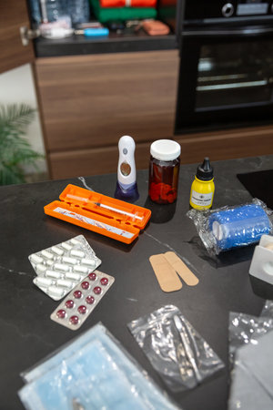Domestic first aid kit ready for injuries or accidents. Medical supplies laying on kitchen including pills, thermometer, disinfectant, bandages, plasters, surgical tape and adhesive band aidsの写真素材