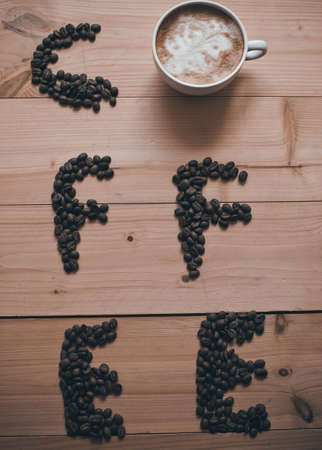 Coffee letters made of coffee beans and cup isolated on wooden backgroundの写真素材