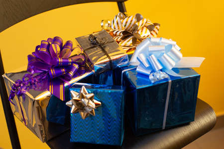 a lot of gifts packed in a bright gift wrapper with bows are lying on a chair. on the background of...