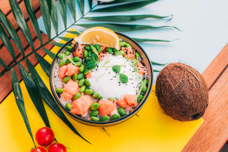 poke bowl with salmon and sauce top view. coconut and tomatoes on the background