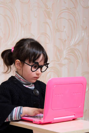 Child in glasses and old clothes is sitting at the laptop