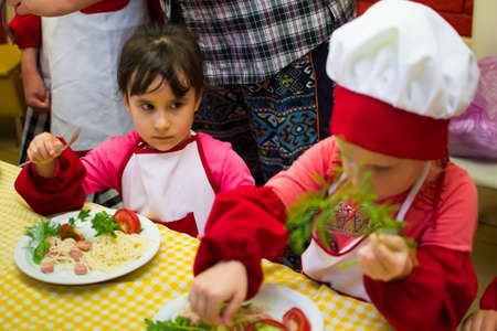 Alchevsk, Ukraine - July 30, 2017: School cooks for children. Learn to cook pasta with sausages -のeditorial素材