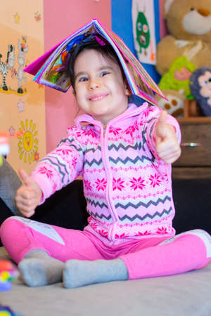 Cute girl on the background of her toys with a bookの写真素材