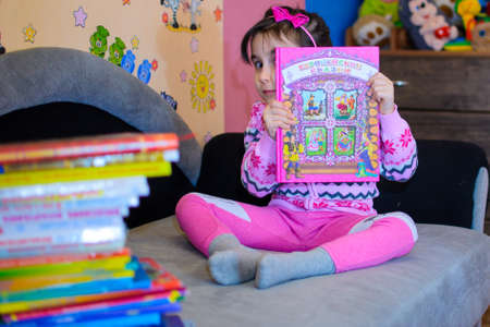 Cute girl on the background of her toys with a bookの写真素材