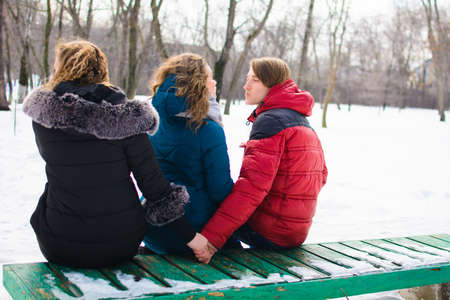 The concept of the image of marital infidelity. Young people on the bench, hugs one and hold the others handの写真素材