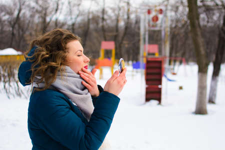 Beautiful young woman in winter park looks in the mirrorの写真素材