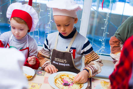 Alchevsk, Ukraine - November 21, 2018: children in the form of cooks prepare pancakes.のeditorial素材