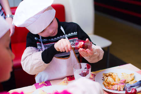 Alchevsk, Ukraine - November 21, 2018: children in the form of cooks prepare pancakes.のeditorial素材