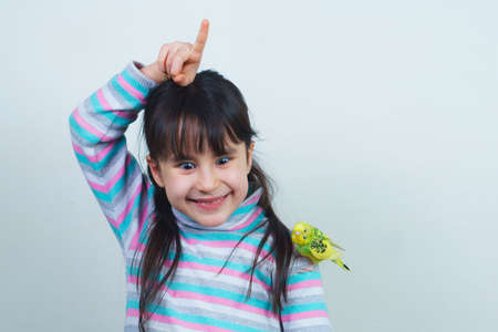 Cool budgie. A cute yellow budgerigar is sitting on the shoulder of a girl with long hair. Tamed Pet