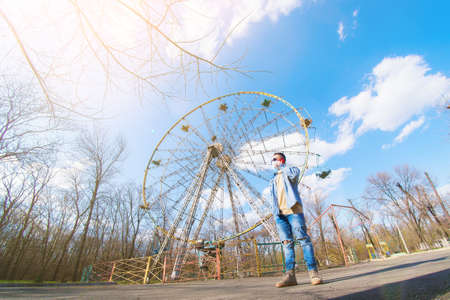 medical mask as protection against coronavirus. guy on the background of an empty ferris wheel in the park speaks on the phoneの写真素材