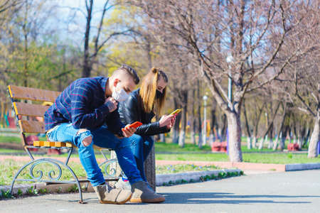 medical mask as protection against coronavirus. a guy and a girl are sitting on a bench at a...