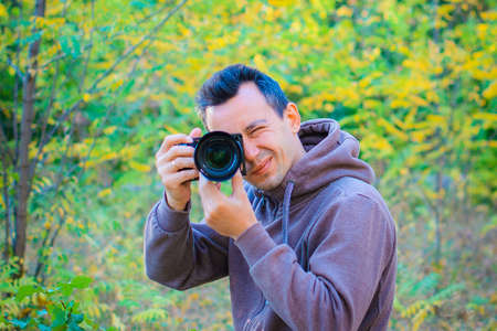A young guy photographer walks through the forest and takes pictures of nature on a dslr camera