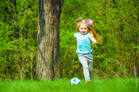 A cute little girl plays with a ball on a green meadow.の写真素材
