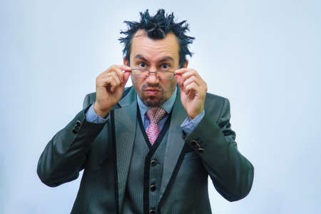 A man with disheveled hair in a business suit adjusts his glasses