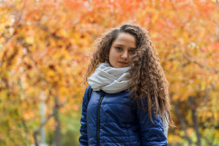 Girl with curly hair in a blue jacket against a background of autumn foliageのeditorial素材
