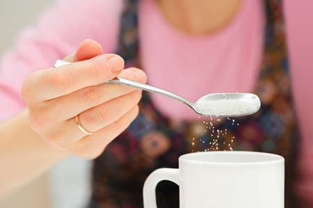 girl holds a spoon and strews sugar to mugの写真素材