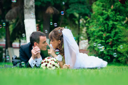 groom and bride lie on a grass around soap bubblesの写真素材