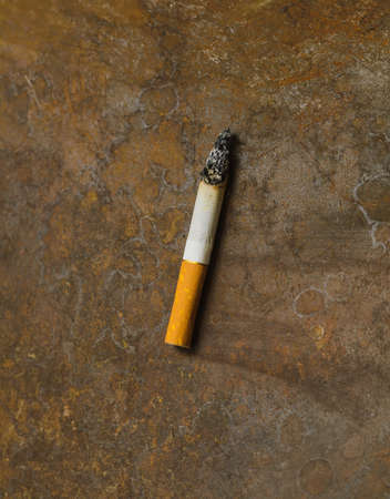 one used burned cigarette on rusty metal backgroundの写真素材