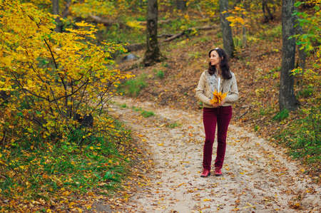 woman with maple autumn leaves standing on forest roadの写真素材