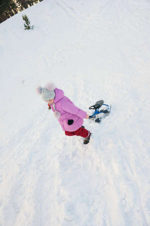 girl go uphill and drag her snow-scooterの写真素材