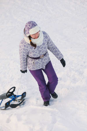 woman go uphill and drag snow-scooter on white snow backgroundsの写真素材