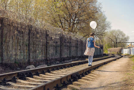 girl with pigtails walk on rails with a balloon on a string in her handの写真素材