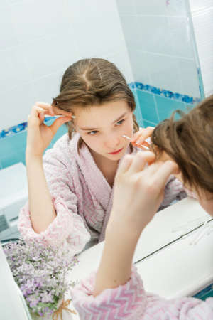sad teenage girl with acne removing pimples with a cotton swab. problems of transition ageの写真素材