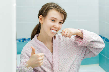 Happy teenage girl looks in the mirror, smiles and brushes her teeth. Prevention of cariesの写真素材