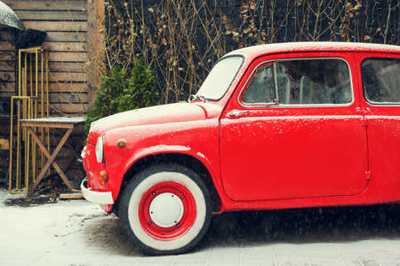 old small car of bright red color stands on the street in winter snow weather. retro tonedの写真素材