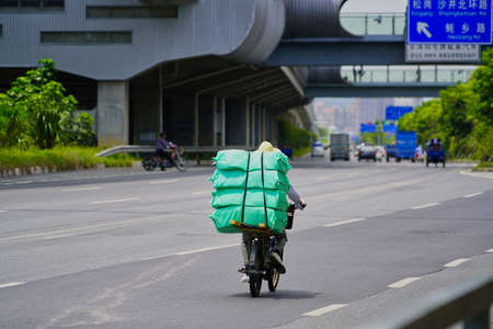 Shenzhen, China - A guy on an old motorcycle carrying a heavy load in a very modern city environment, quite contrastingの写真素材