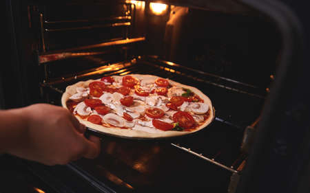 The hand of the chef immerses the raw pizza billet in the oven for further bakingの写真素材