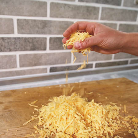 Cook's hand pours crushed yellow cheese onto a wooden boardの写真素材