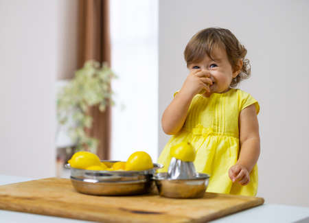 A little girl in a yellow dress sniffs lemon with pleasure.の写真素材