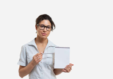 Portrait of a young beautiful woman in glasses with a pencil and a notepad on white backgroundの写真素材