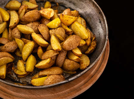 Golden potatoes in cast iron skillet on wooden boardの写真素材