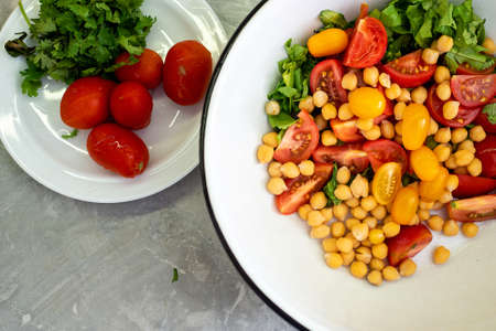A bowl of salad ingredients, next to a plate of tomatoesの写真素材