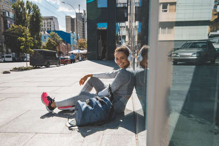 The athlete sits with his back against a glass wall, listens to music and smilesの写真素材