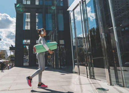 An athlete in white headphones with a green mat comes to the entrance to the buildingの写真素材