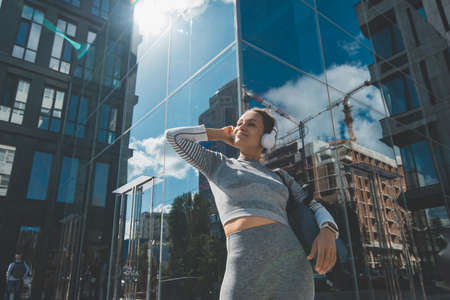 Young woman closing her eyes pretty listening to music on the background of a modern buildingの写真素材
