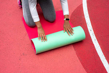 The young woman with hands spreads green mat while kneeling