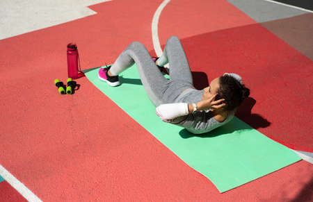 The young woman in gray tracksuit doing abdominal exercise while lying down