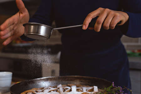 Preparation, Thanksgiving Day celebration. Making a traditional apple pie. A cook sprinkles the surface of the finished cake with powdered sugar and a steel strainer.の写真素材